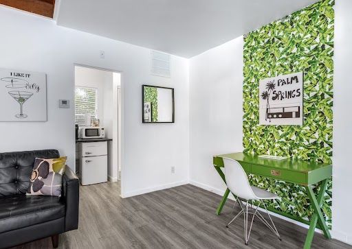 Modern living room with white walls, green leaf accent wall, black sofa, and small desk with chair