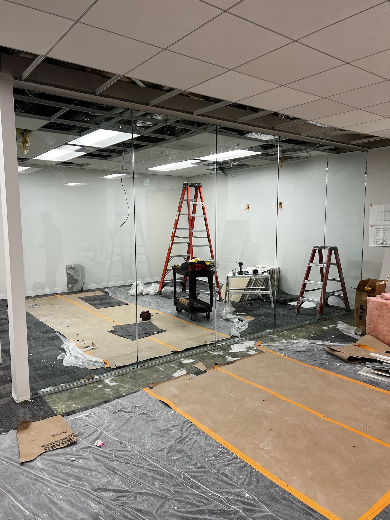 Office space undergoing renovation with exposed ceiling, ladders, and debris on the floor.