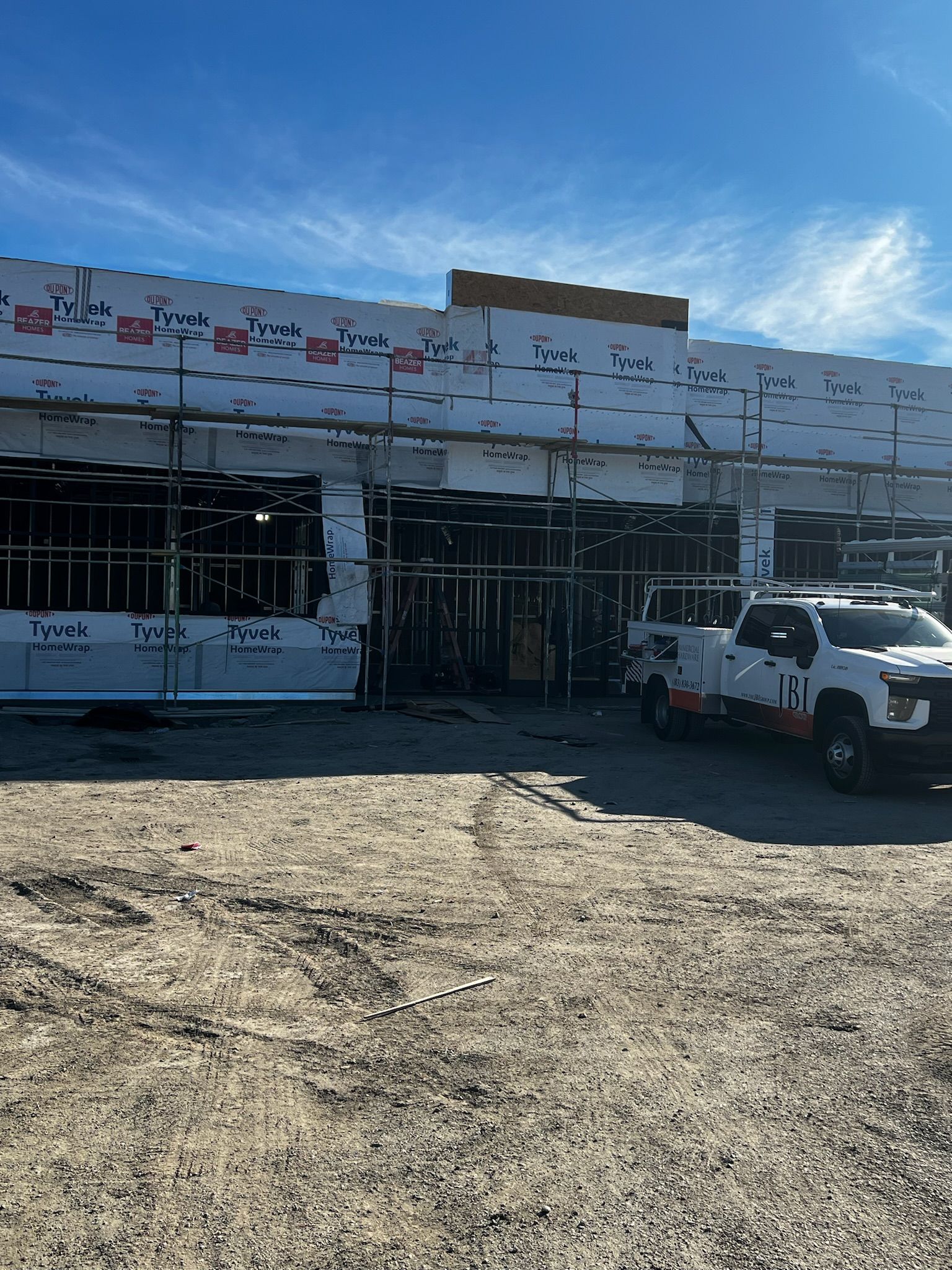 Building under construction with scaffolding and a truck parked outside on a dirt lot.