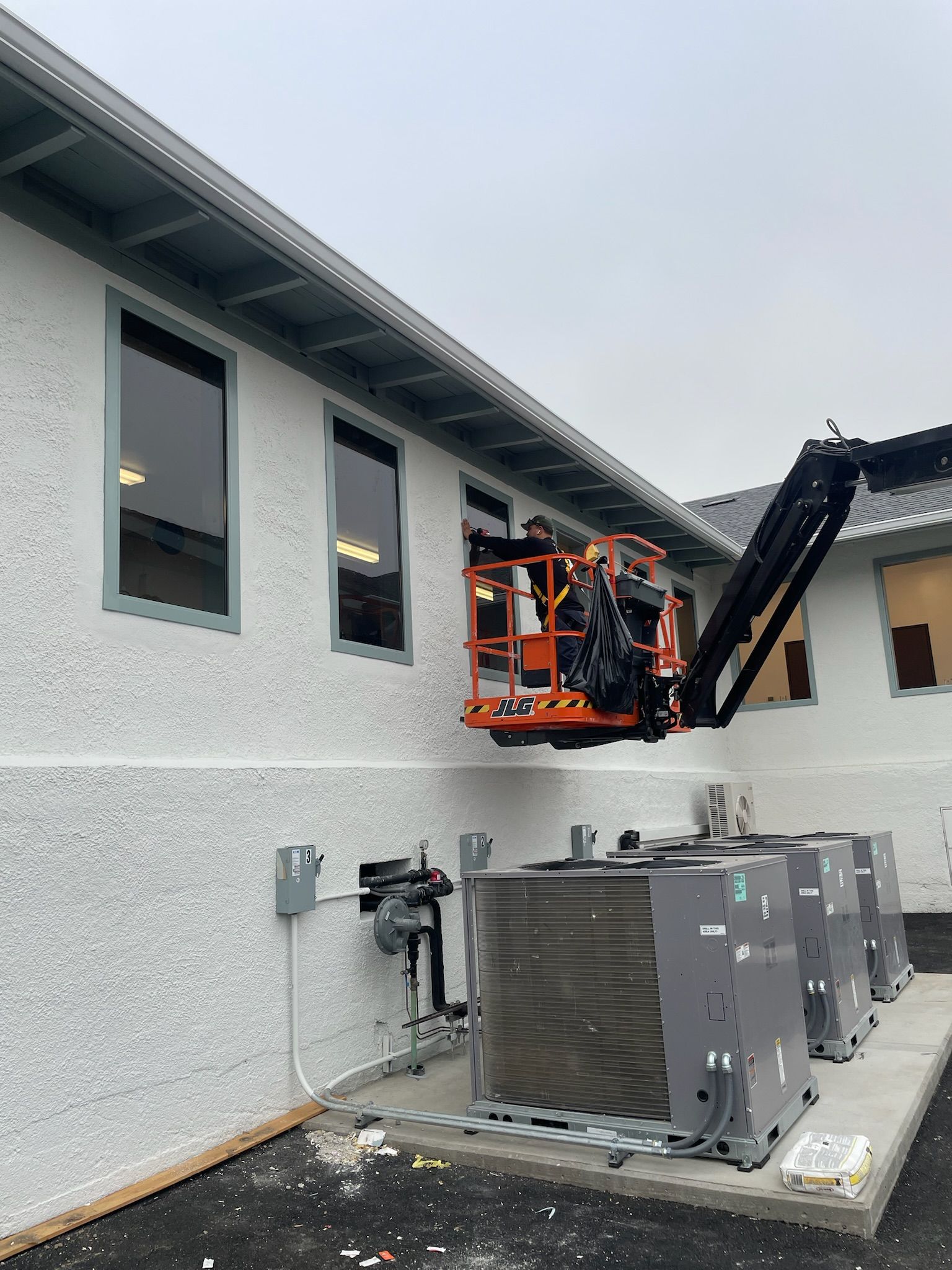 Workers in a lift working on a building's exterior near windows. Grey, white, and orange equipment.