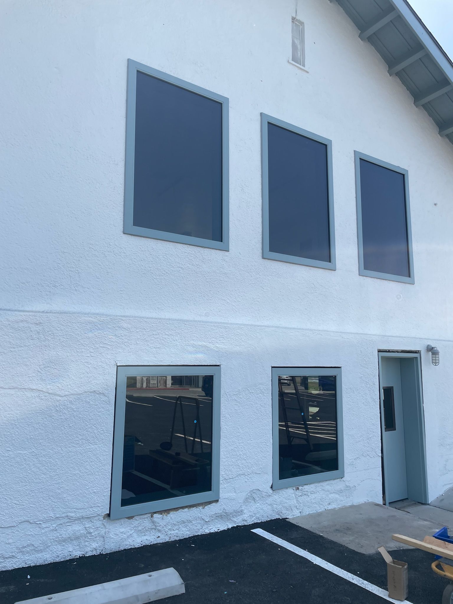 White building with dark tinted windows, gray trim. Entrance door. Black asphalt.