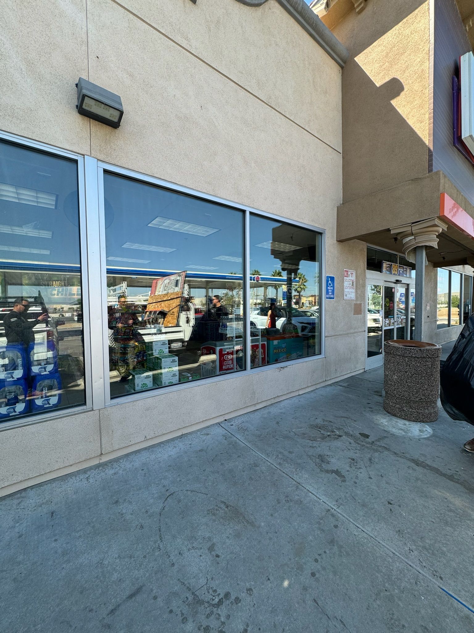 Storefront with large windows reflecting sky and goods inside. Paved walkway.
