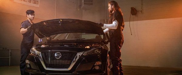 Dos personas de pie junto a un SUV Nissan negro bajo una cálida iluminación de estudio.