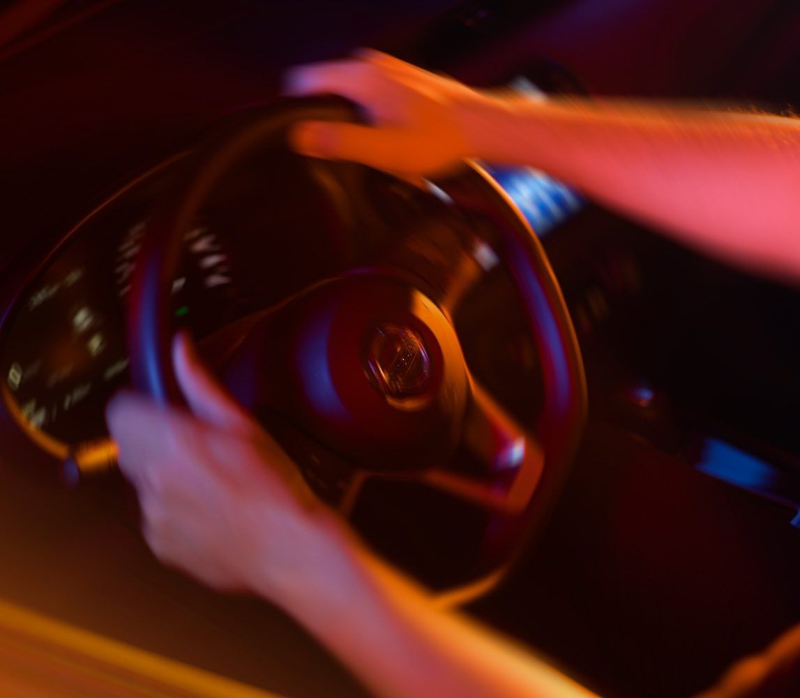 Manos agarrando un volante en el interior de un coche con poca luz y una iluminación cálida de color rojo anaranjado.