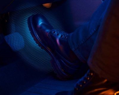 Primer plano iluminado con luz azul de zapatos de vestir negros pulidos y perneras de pantalón sobre un asiento estampado.