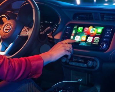 Una persona con una camisa roja extiende la mano hacia el panel de control táctil de un automóvil por la noche.