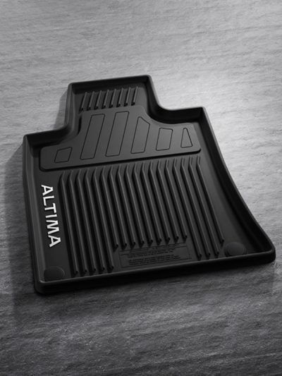 Alfombrilla de coche negra moldeada con la etiqueta “ALTI MA” sobre una superficie gris.