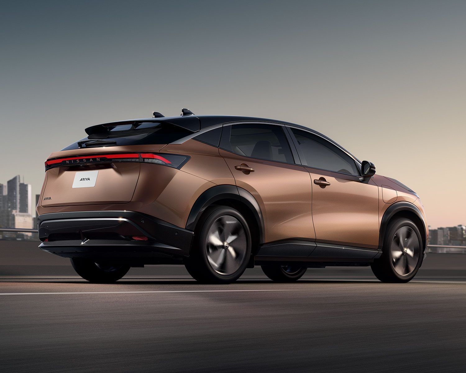 Un SUV color bronce circula por una carretera con el perfil de la ciudad al fondo.