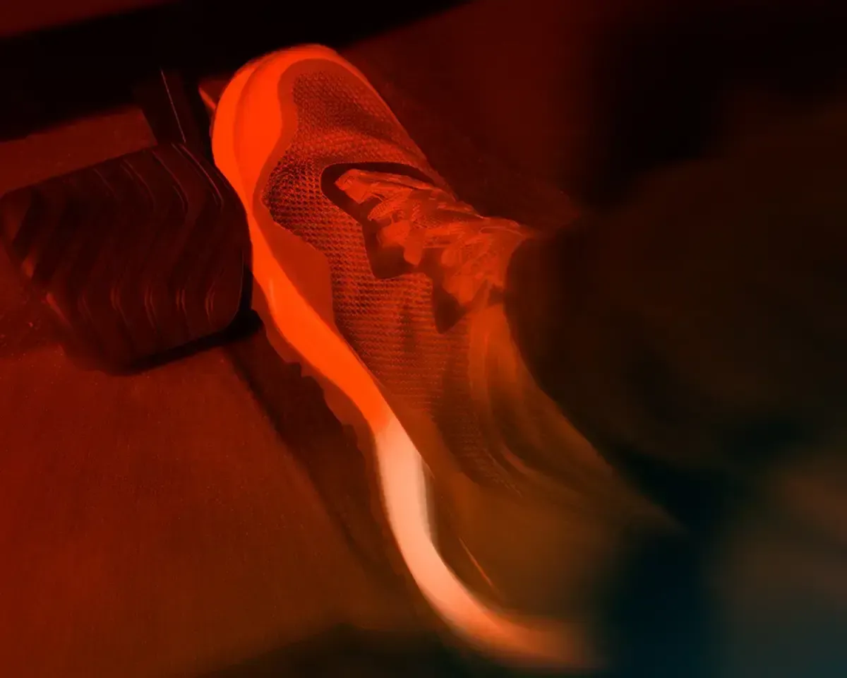 Una zapatilla roja en movimiento bajo iluminación roja, con una pierna borrosa y un fondo oscuro.