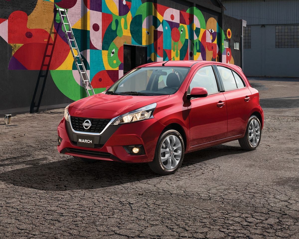 Un Nissan hatchback rojo estacionado en la acera frente a un colorido mural.