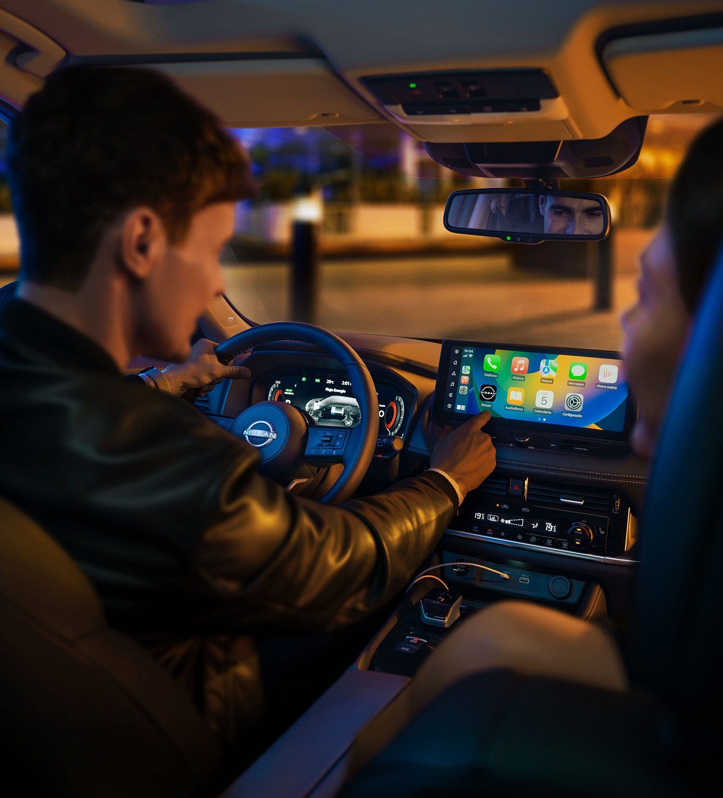 Conductor utilizando la pantalla del salpicadero del coche por la noche, vista desde el asiento trasero.