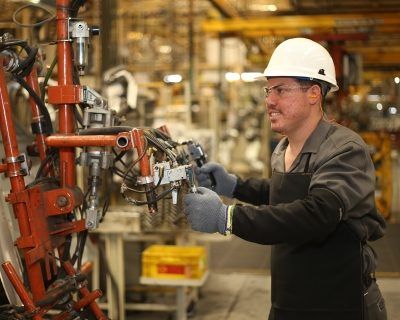 Trabajador con casco operando maquinaria industrial en un entorno de fábrica.