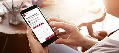 Persona usando un teléfono inteligente en una mesa, viendo una pantalla de aplicación roja y blanca.