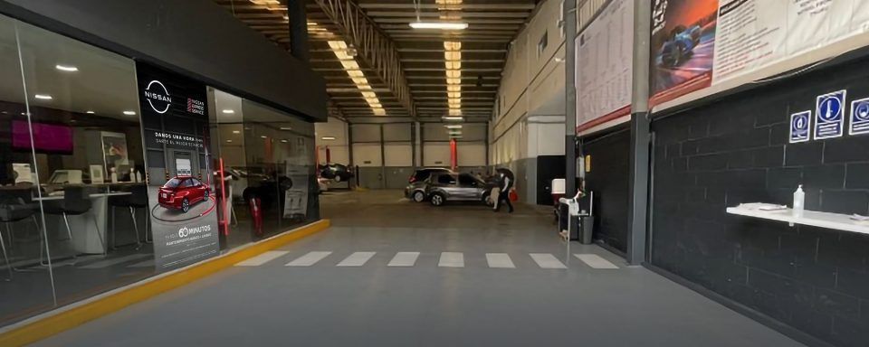 Entrada a un estacionamiento cubierto con líneas de paso de peatones, autos estacionados y una escalera al fondo.
