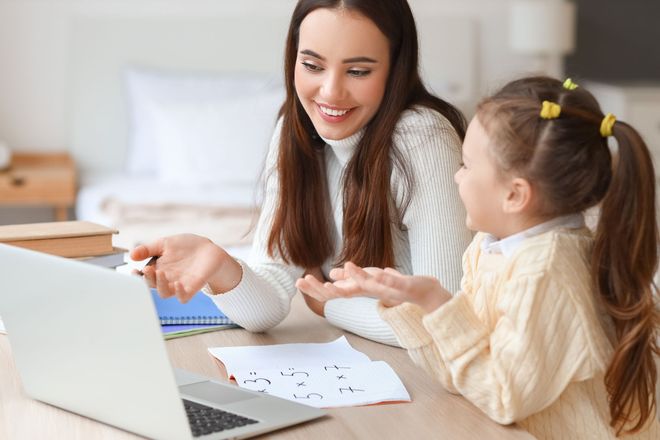 A woman and a little girl are sitting at a table looking at a laptop.
