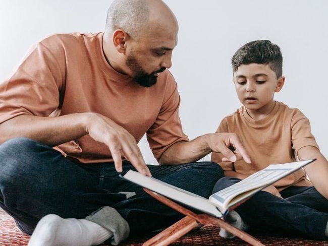 A man and a boy are sitting on the floor reading a book.