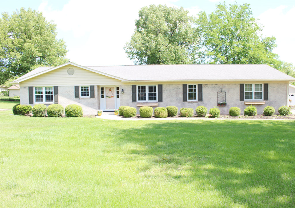 A white house with black shutters is sitting on top of a lush green field.