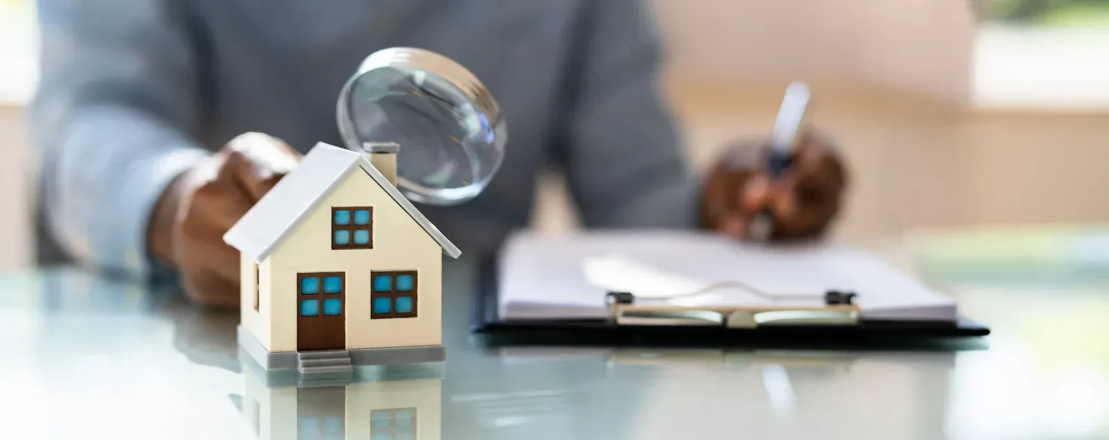 A man is sitting at a table with a magnifying glass and a model house.