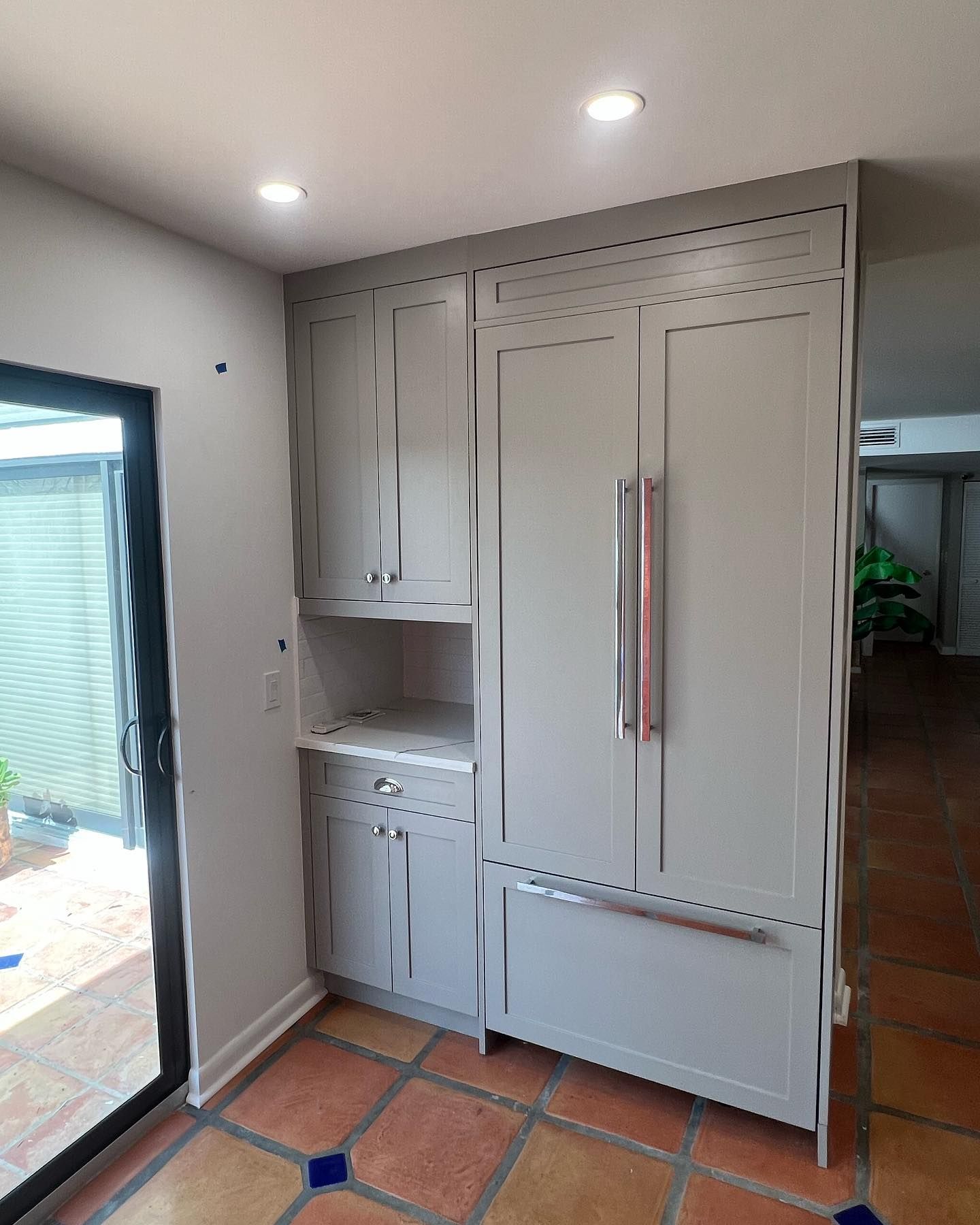 Gray kitchen cabinetry with built-in refrigerator, near a doorway and tiled floor.
