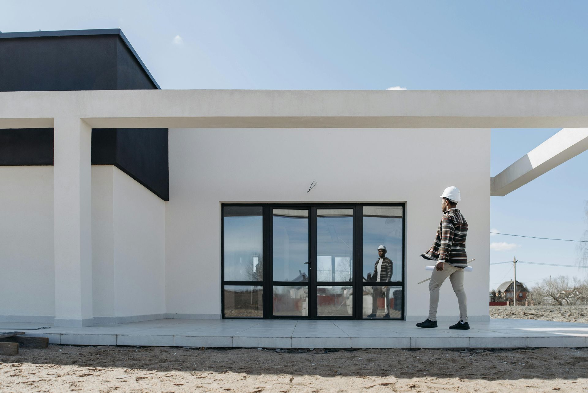 Construction worker in hard hat walks by modern white building, holding blueprints.