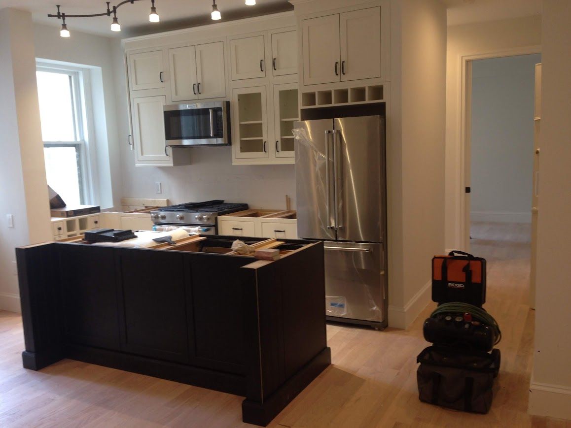 Kitchen under construction with black island, white cabinets, stainless steel appliances, and wooden floor.
