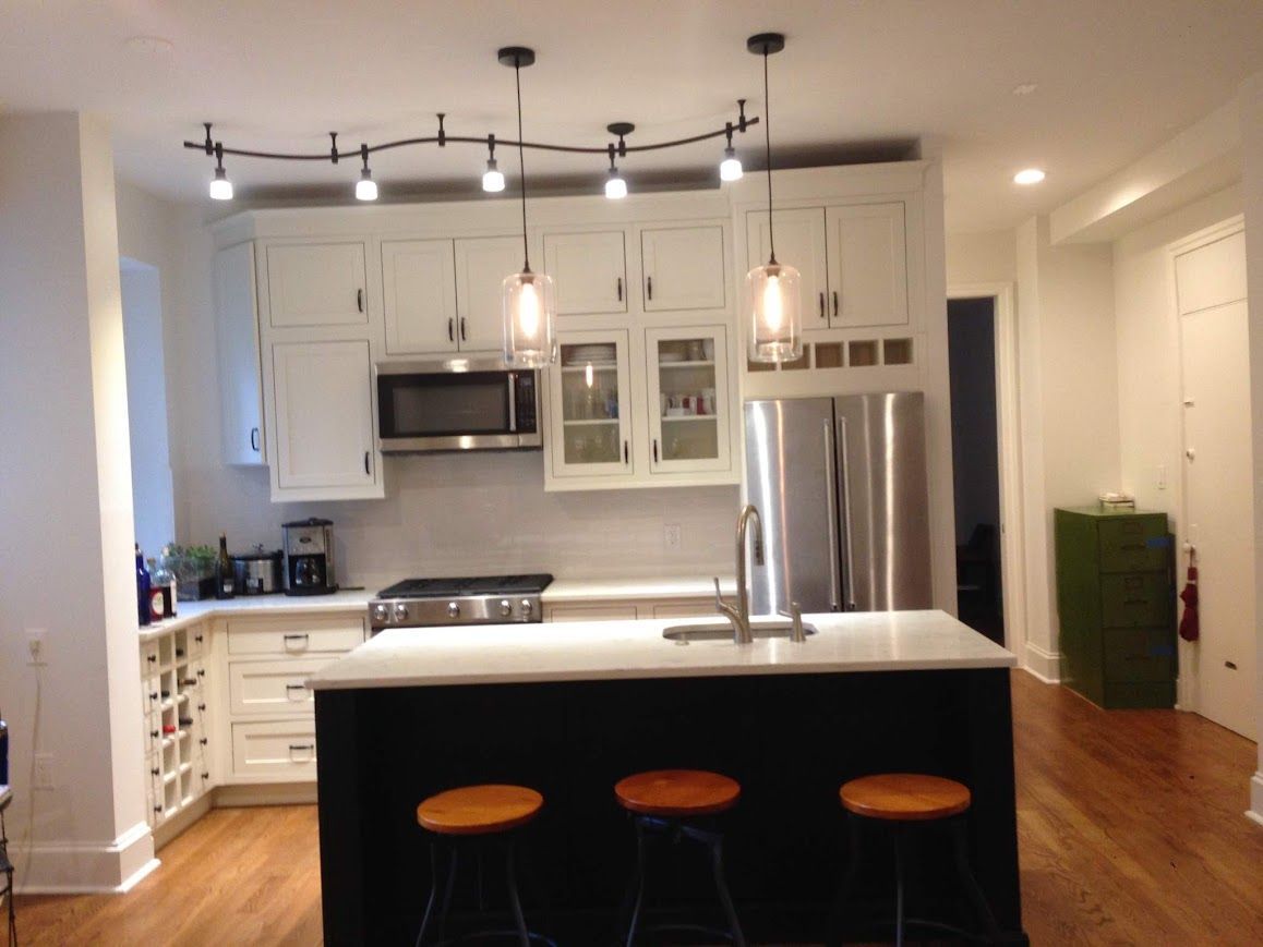 Kitchen with white cabinets, island with stools, and overhead lighting.
