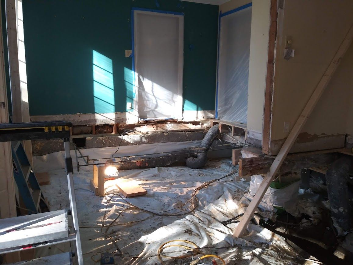 Room under renovation with exposed floor and damaged walls, green paint, and construction materials.