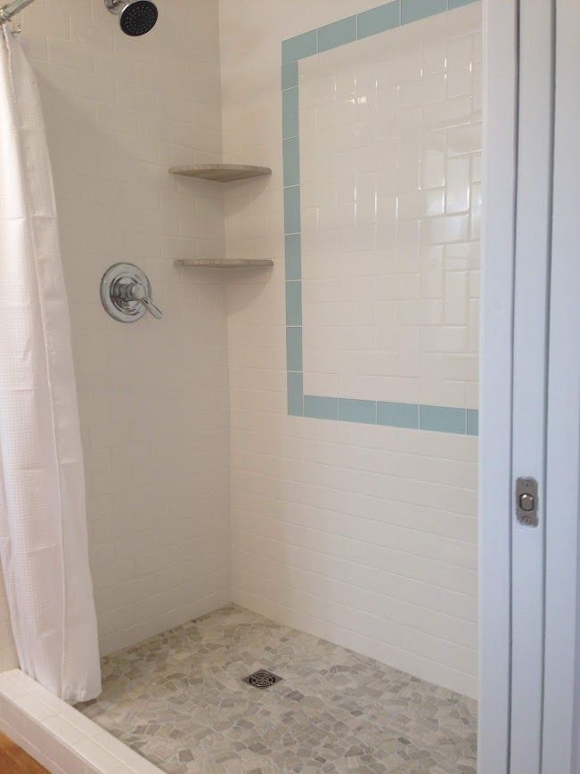 Shower with white walls, blue tile border, and stone floor. Features built-in shelves and a curtain.