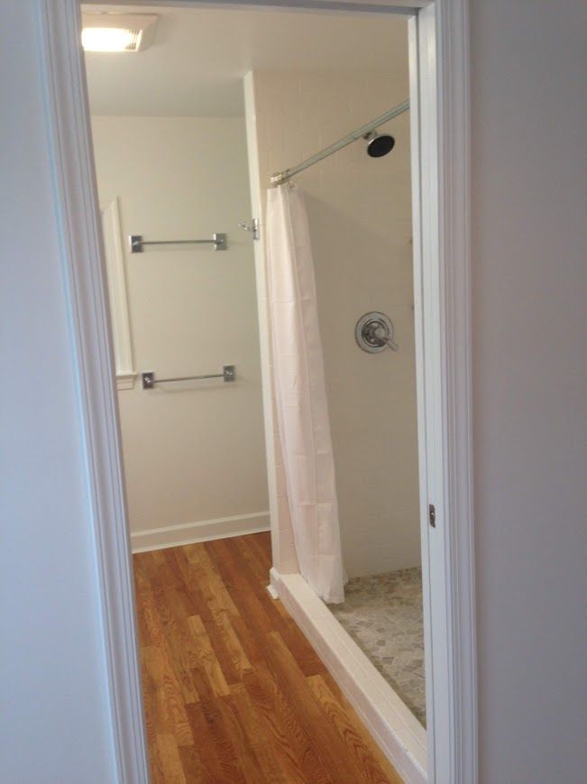 View through doorway into bathroom: shower with curtain, towel racks, and wood floor.
