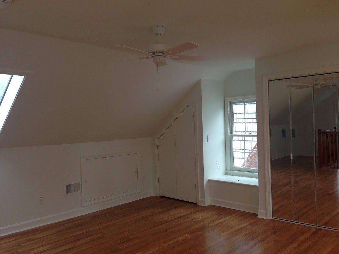 Empty room with slanted ceiling, hardwood floor, window, closet, and ceiling fan.