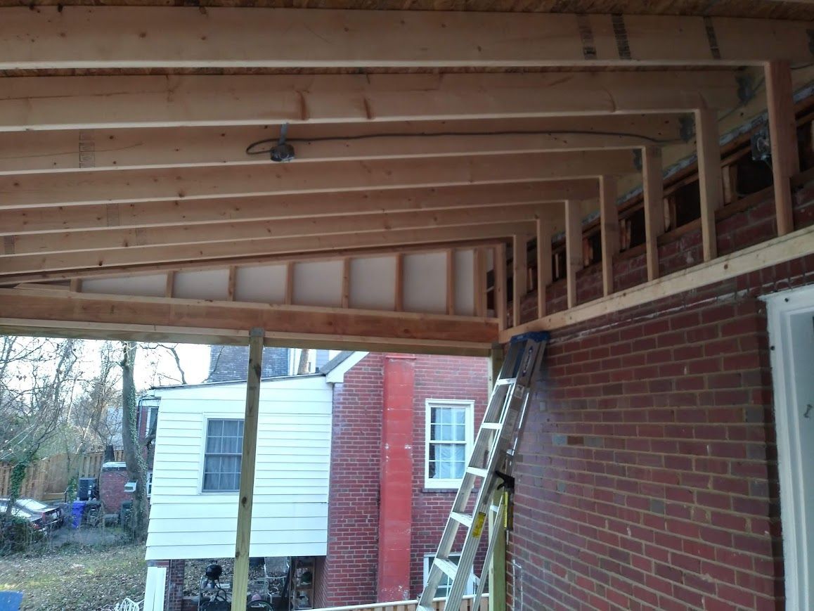 Construction of a porch roof, including wooden beams and partially built walls, on a brick building with a ladder present.