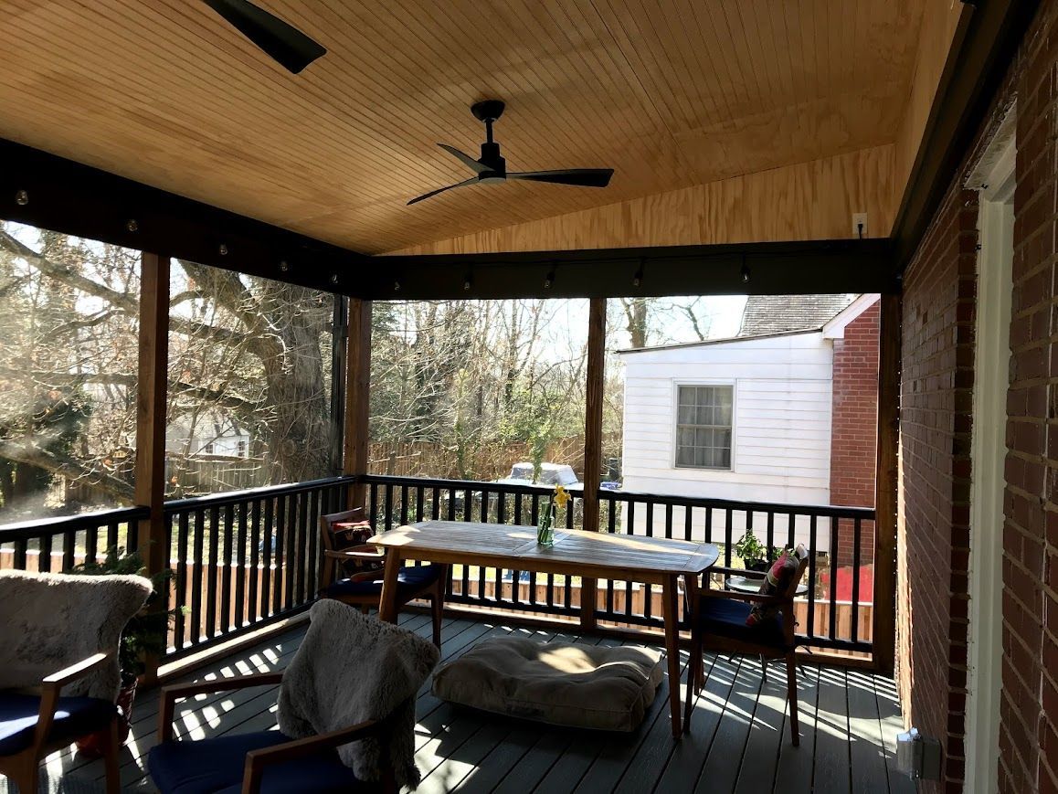Screened-in porch with table, chairs, and ceiling fan; overlooking yard with trees and a small white building.