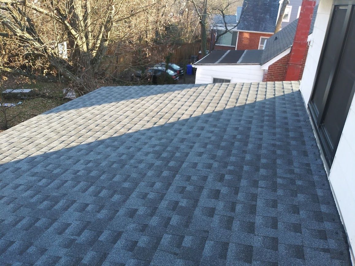 Dark gray asphalt shingle roof. View from above with other houses and trees in the background.