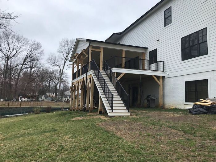 A two-story screened porch with stairs attached to a white building. Construction debris is nearby.