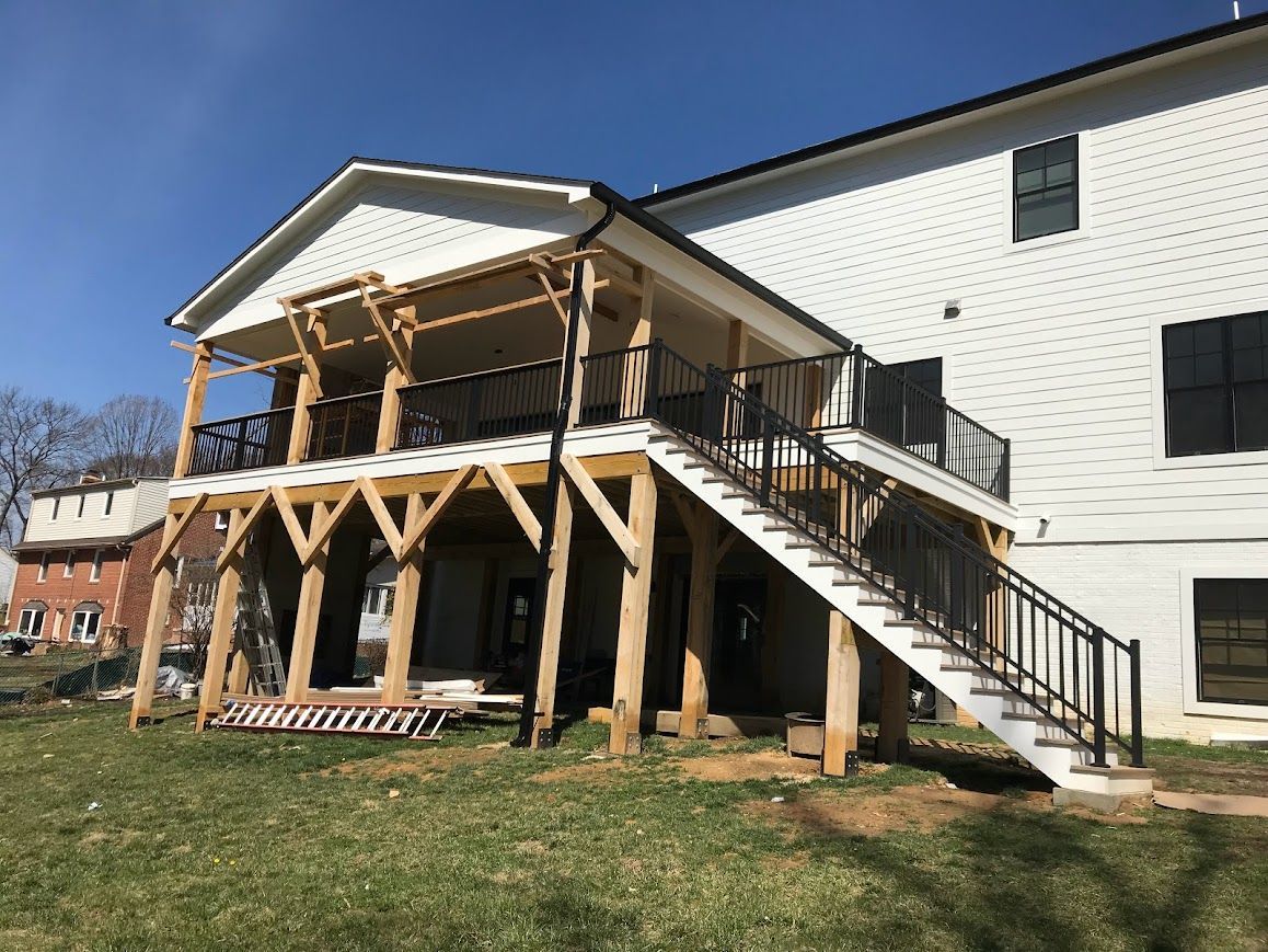 Wooden deck and stairs attached to a white house with black railing.