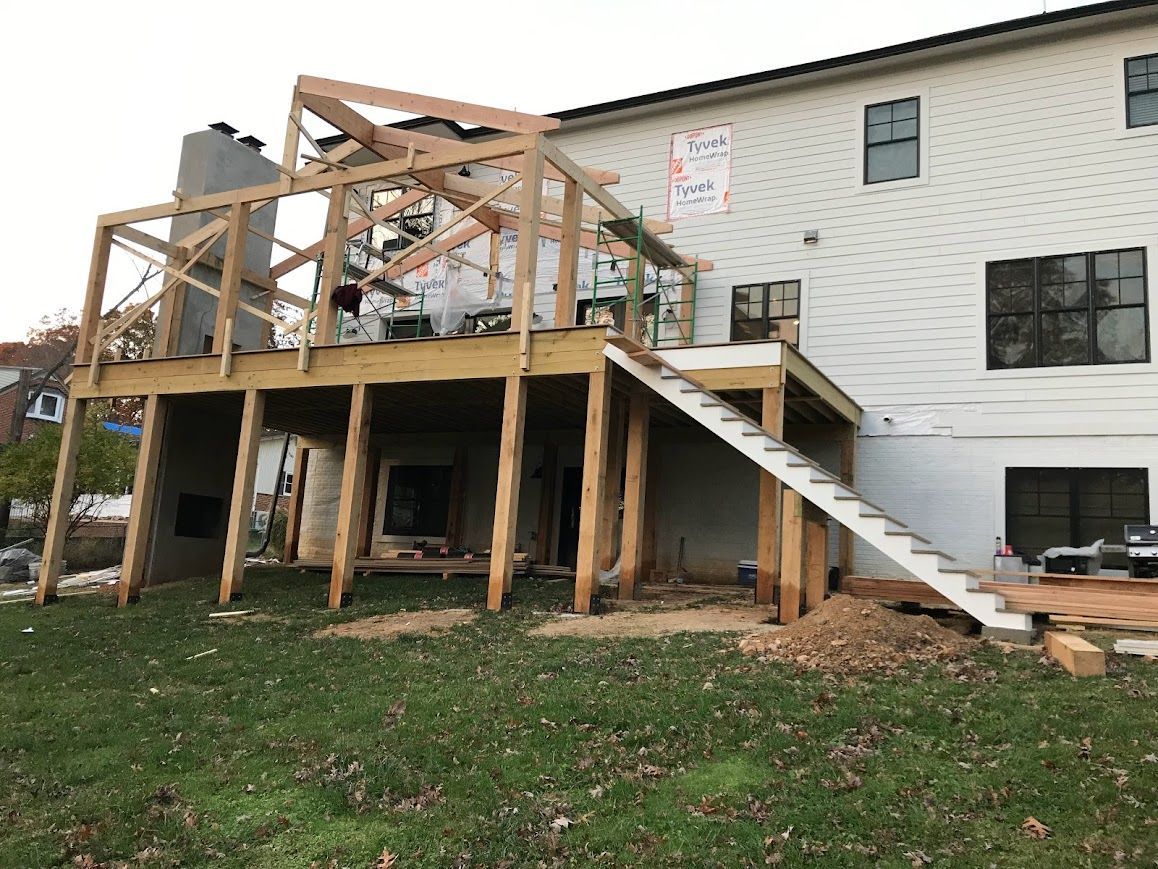 A deck under construction with a staircase attached to a two-story home with white siding.