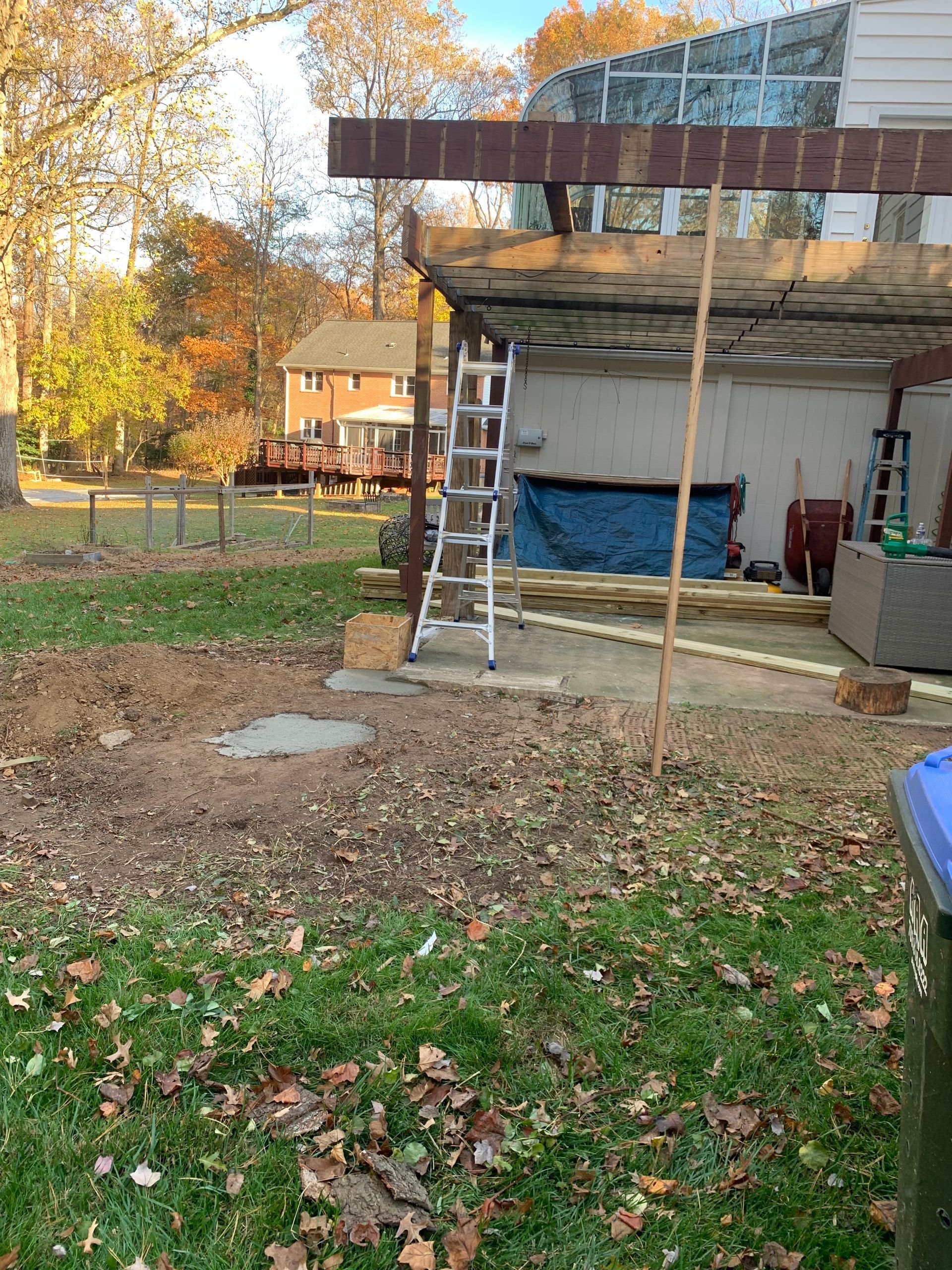 Backyard with construction: deck, ladder, dirt, and foliage, autumn colors.