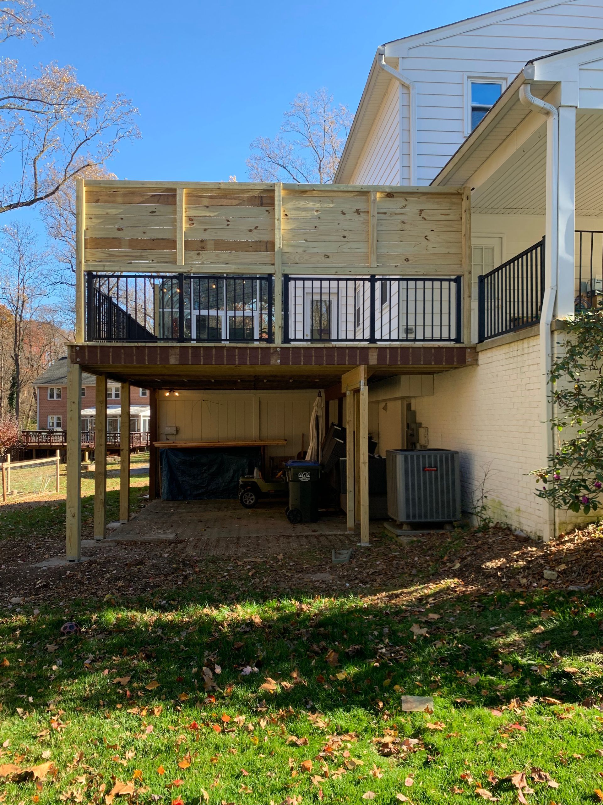 Wooden deck with black railings and a privacy screen attached to a two-story house.