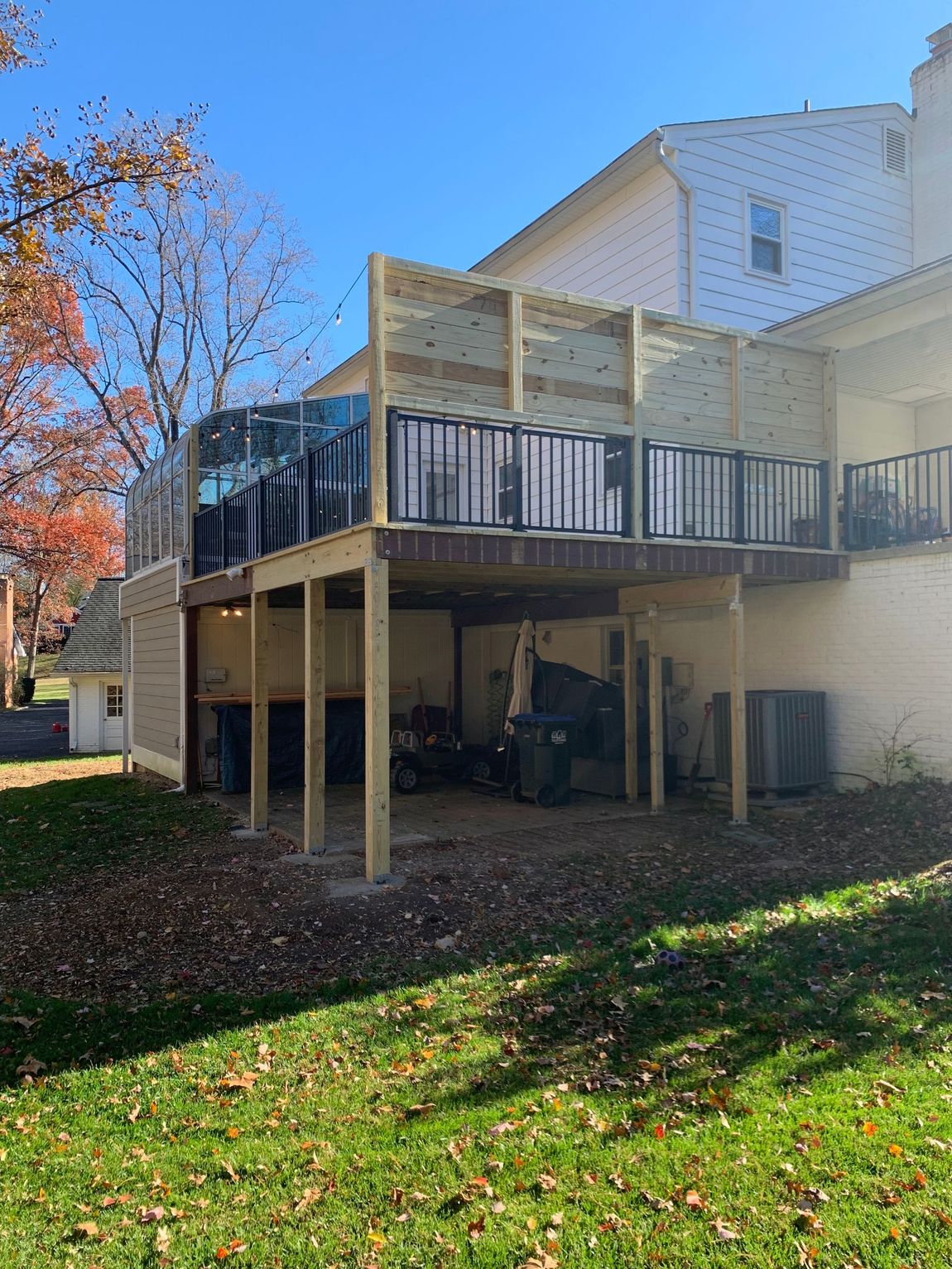 Wooden deck with black railings attached to a white brick house, supported by posts, view from the yard.