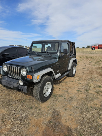 A dark grey Jeep Wrangler parked on dry, grassy terrain under a blue sky with light clouds.