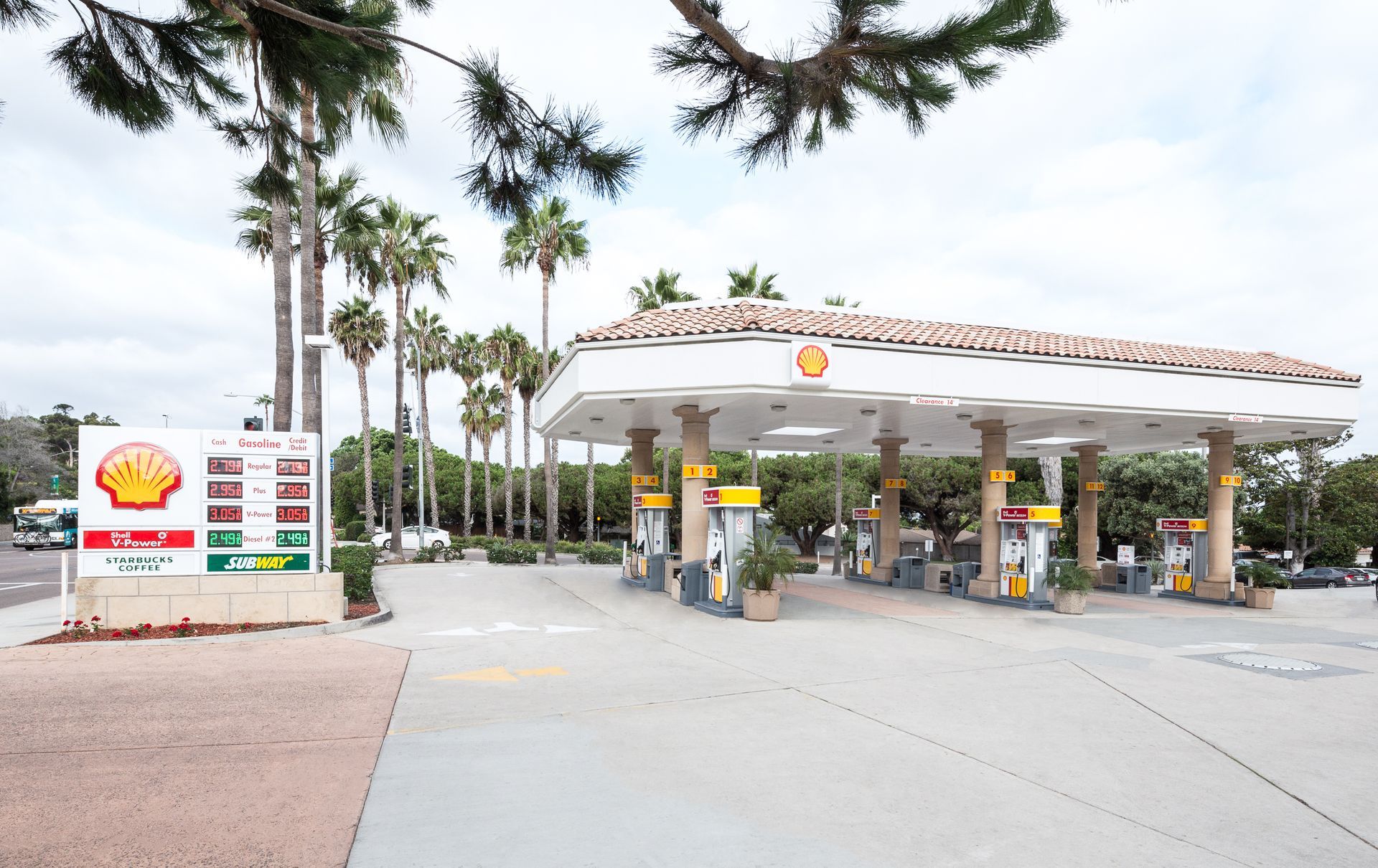 Shell gas station canopy with pumps and palm trees on a cloudy day