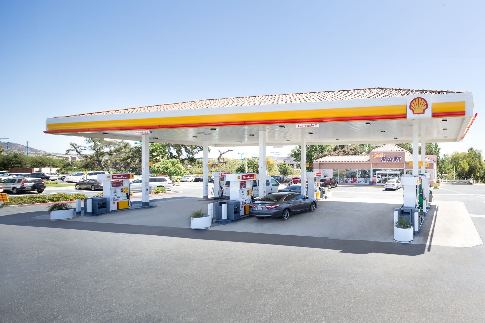 Shell gas station with a wide canopy, pumps, and a few cars on a sunny day