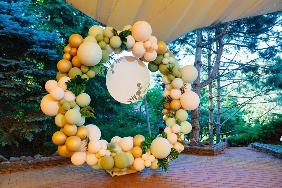 Balloon wreath with white and gold balloons hanging outdoors in a forest-like venue under a tent