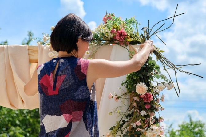 Person arranging flowers on an outdoor arch under a bright blue sky