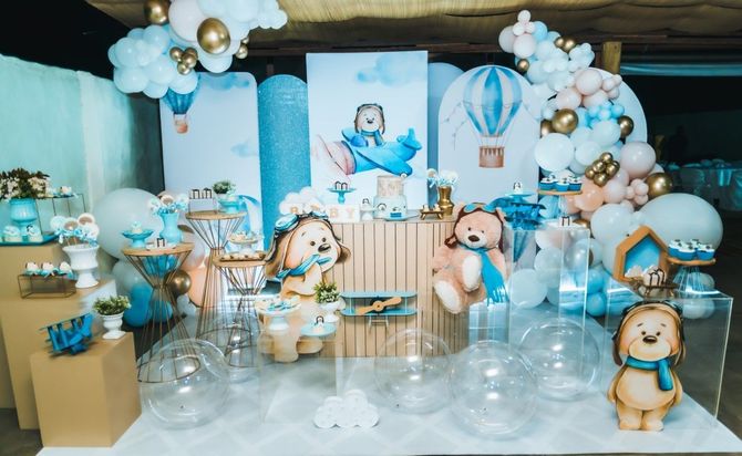 Blue-and-white baby shower dessert table with teddy bears, balloons, clouds, and a central baby illustration
