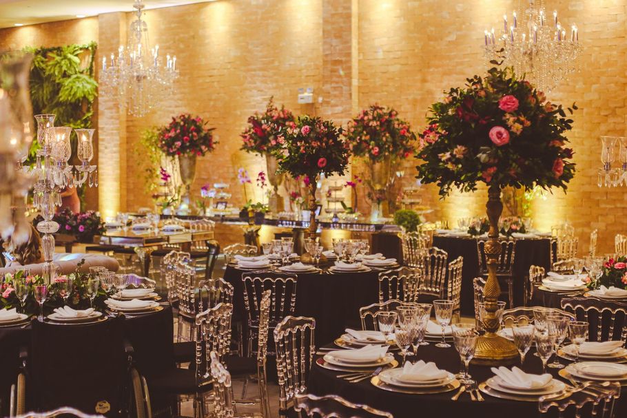 Elegant banquet hall with round tables, crystal chairs, and tall pink floral centerpieces under warm lighting