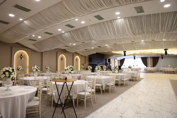 Elegant banquet hall with round tables, white chairs, and draped ceiling lighting in a spacious event venue