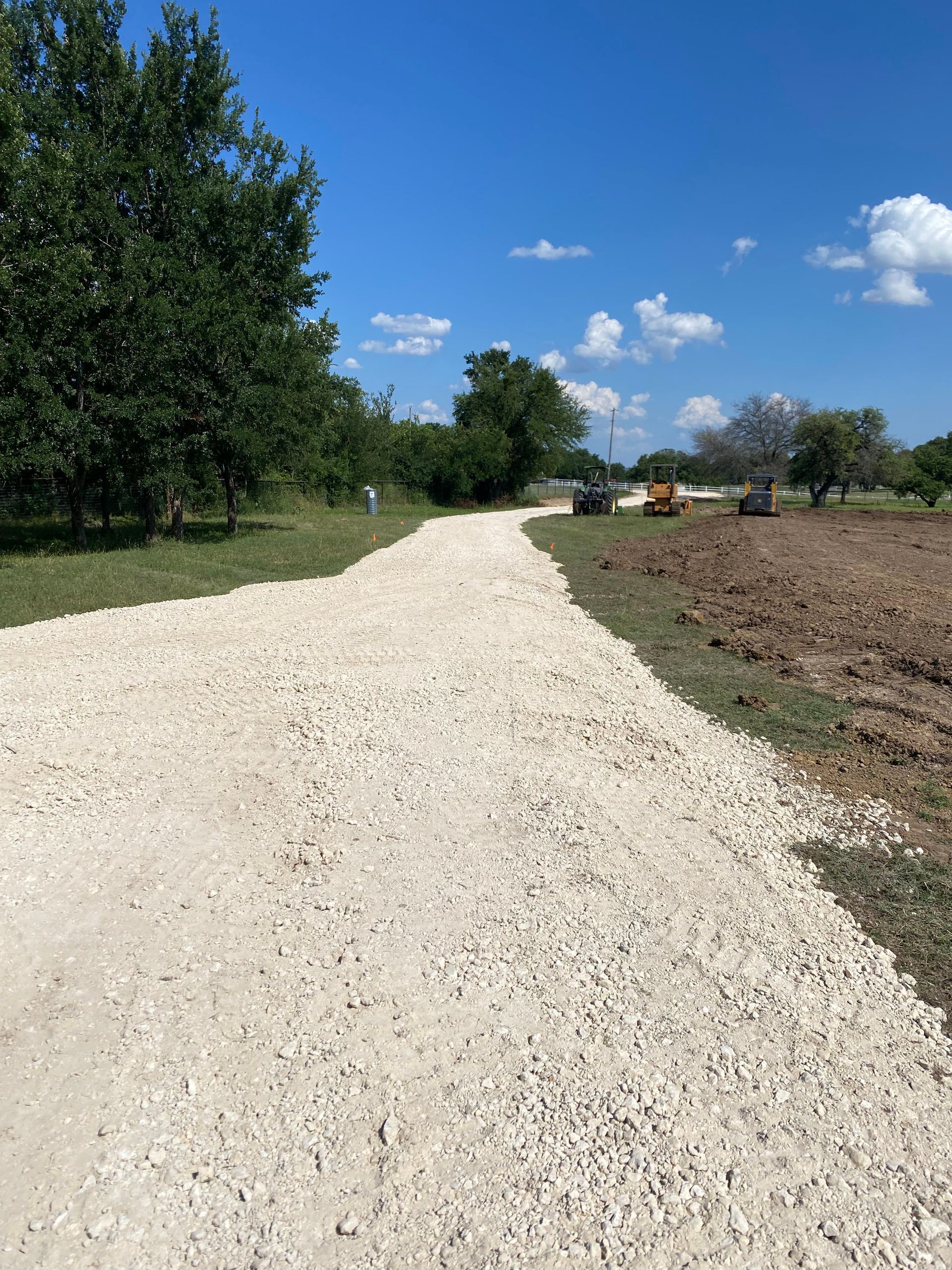 A gravel road going through a field with trees on both sides.