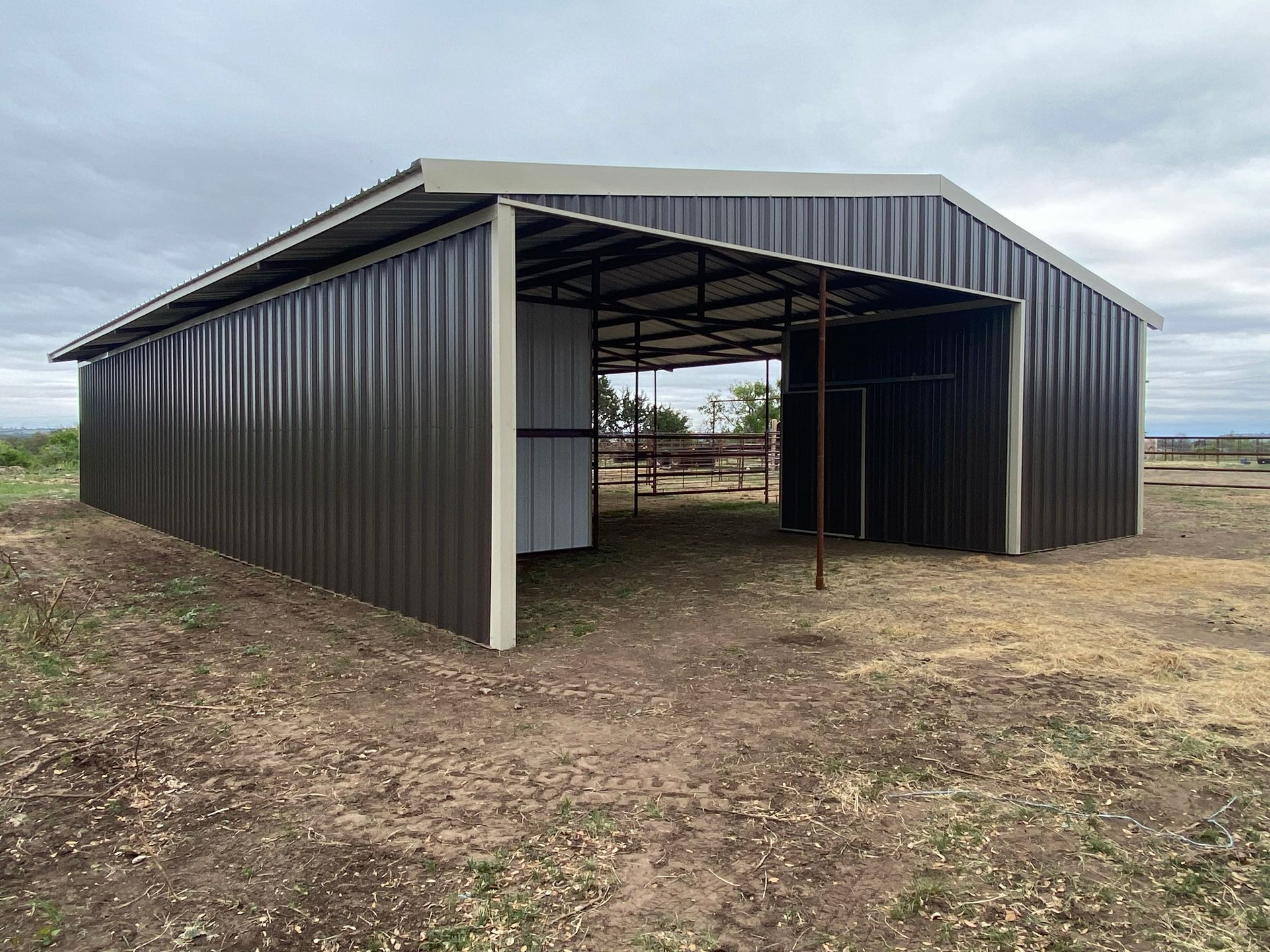 A large metal barn is sitting in the middle of a dirt field.