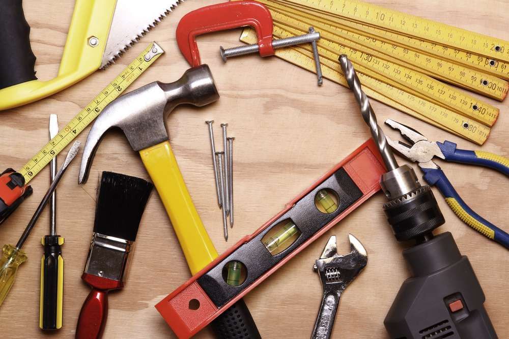 A bunch of tools on a wooden table including a hammer and drill